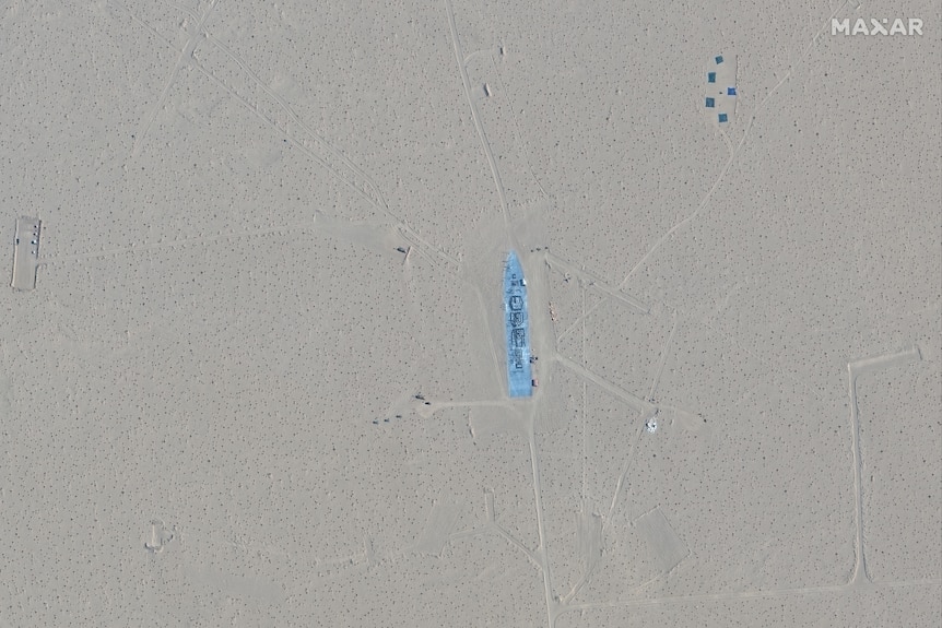 a distant satellite image of a navy vessel-shaped object surrounded by sand in a desert 