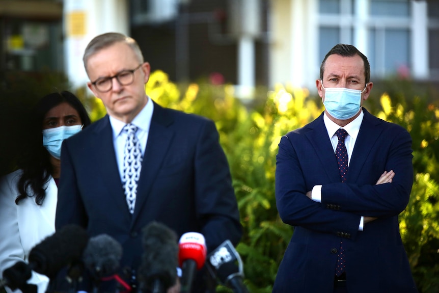 A wide shot showing Mark McGowan watching on wearing a face mask as Anthony Albanese appears at a media conference.