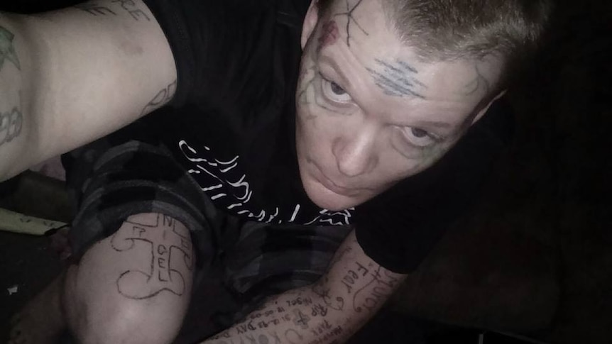 A man with tattoos and short hair, wearing a black t-shirt.
