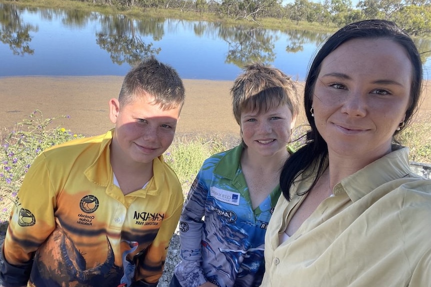 (L-R) Fletcher Gray, Baxter Russ and Jess Gilmour stand on a levee bank next to Gum Creek in Moulamein
