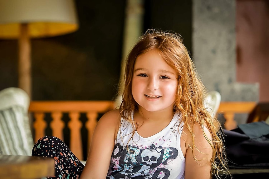 A young girl Belle Cooper is sitting down and smiling.