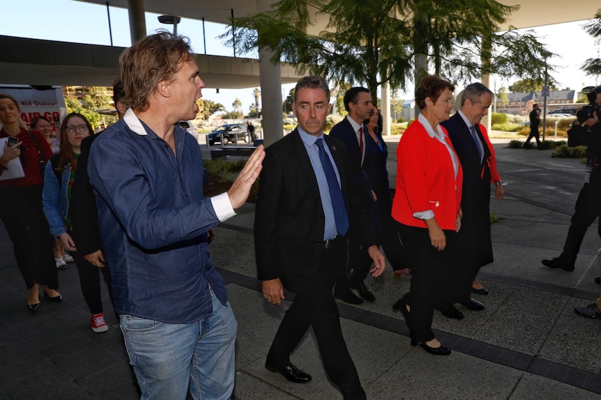 A security guard looks at a heckler who is shouting at Bill Shorten and his Labor entourage as they arrive at a hospital