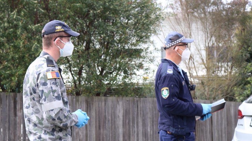 A police officer stands near another man outside, speaking to the media.