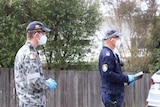 A police officer stands near another man outside, speaking to the media.