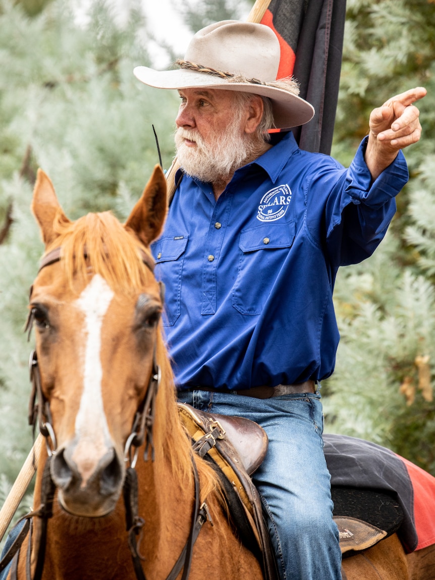 Mountain cattleman Charlie Lovick on a horse holding the Indigenous flag.