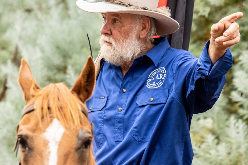 Mountain cattleman Charlie Lovick on a horse holding the Indigenous flag.