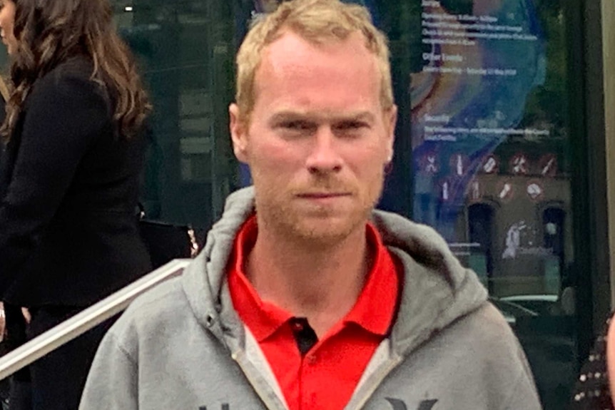 Brian Jackson, who has blonde hair and has a neutral expression on his face, walks out of a court house.