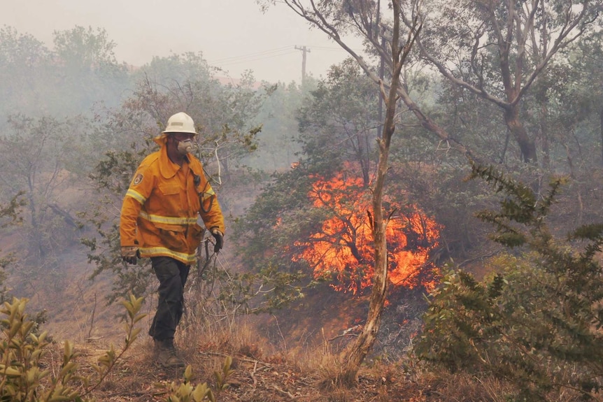 A firefighter with a blaze behind him.