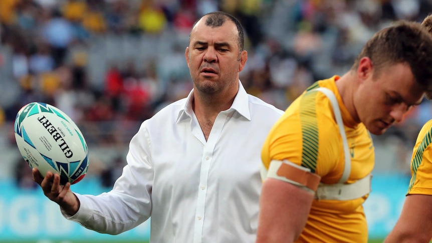 Michael Cheika holds a rugby ball as players look to the turf during a pre-match warm-up