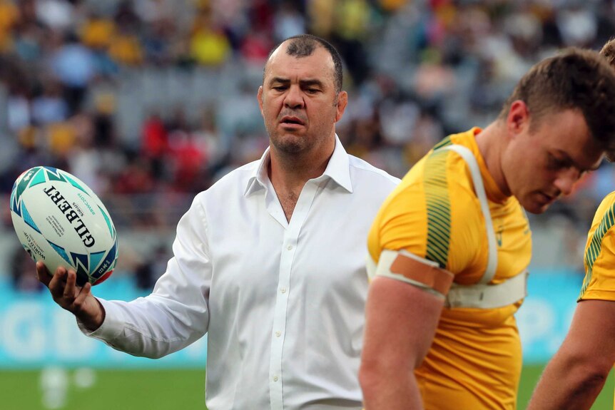 Michael Cheika holds a rugby ball as players look to the turf during a pre-match warm-up