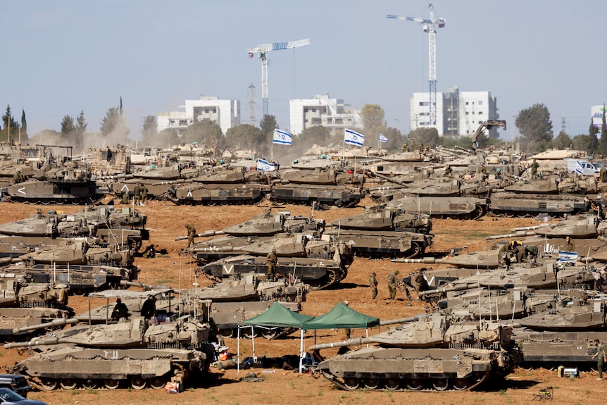 Multiple tanks at on a desert area with a cityscape in the background.