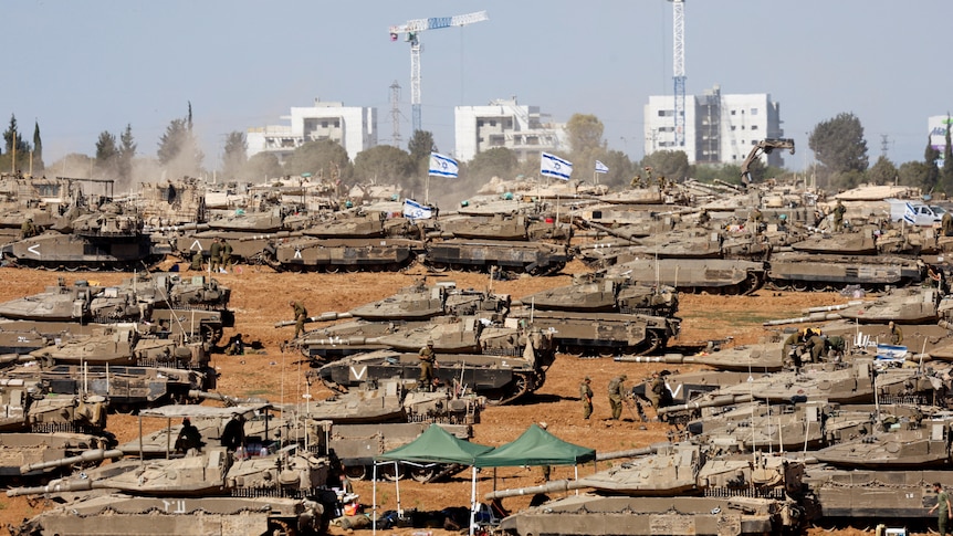 Multiple tanks at on a desert area witha  city scape in the background. 
