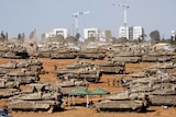 Multiple tanks at on a desert area witha  city scape in the background. 