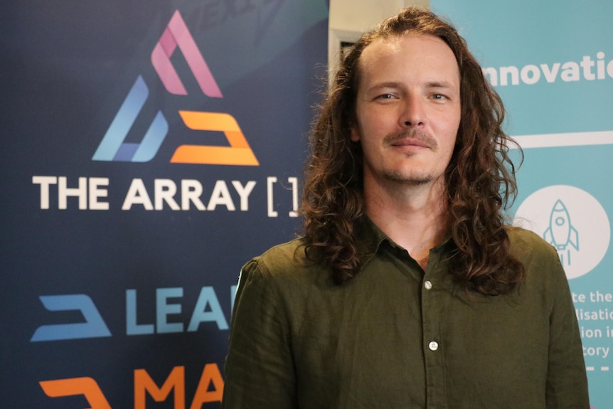 A man with long hair standing next to a sign for The Array.