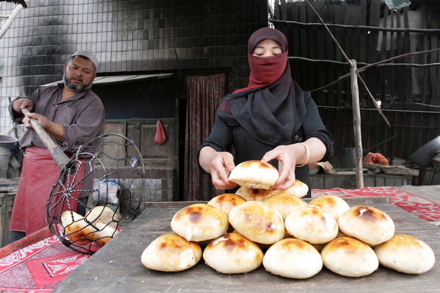 Man passes freshly baked bread to woman who piles loaves on a market bench