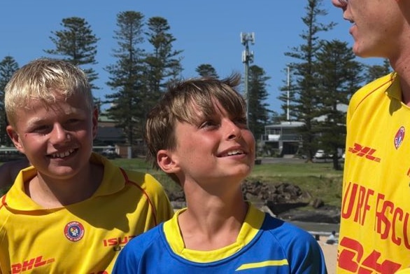 two young boys, one in surf life saving yellow look at older boy