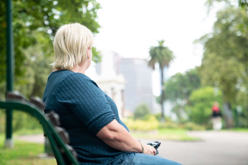 The profile of a middle-aged blonde woman sitting on a park bench