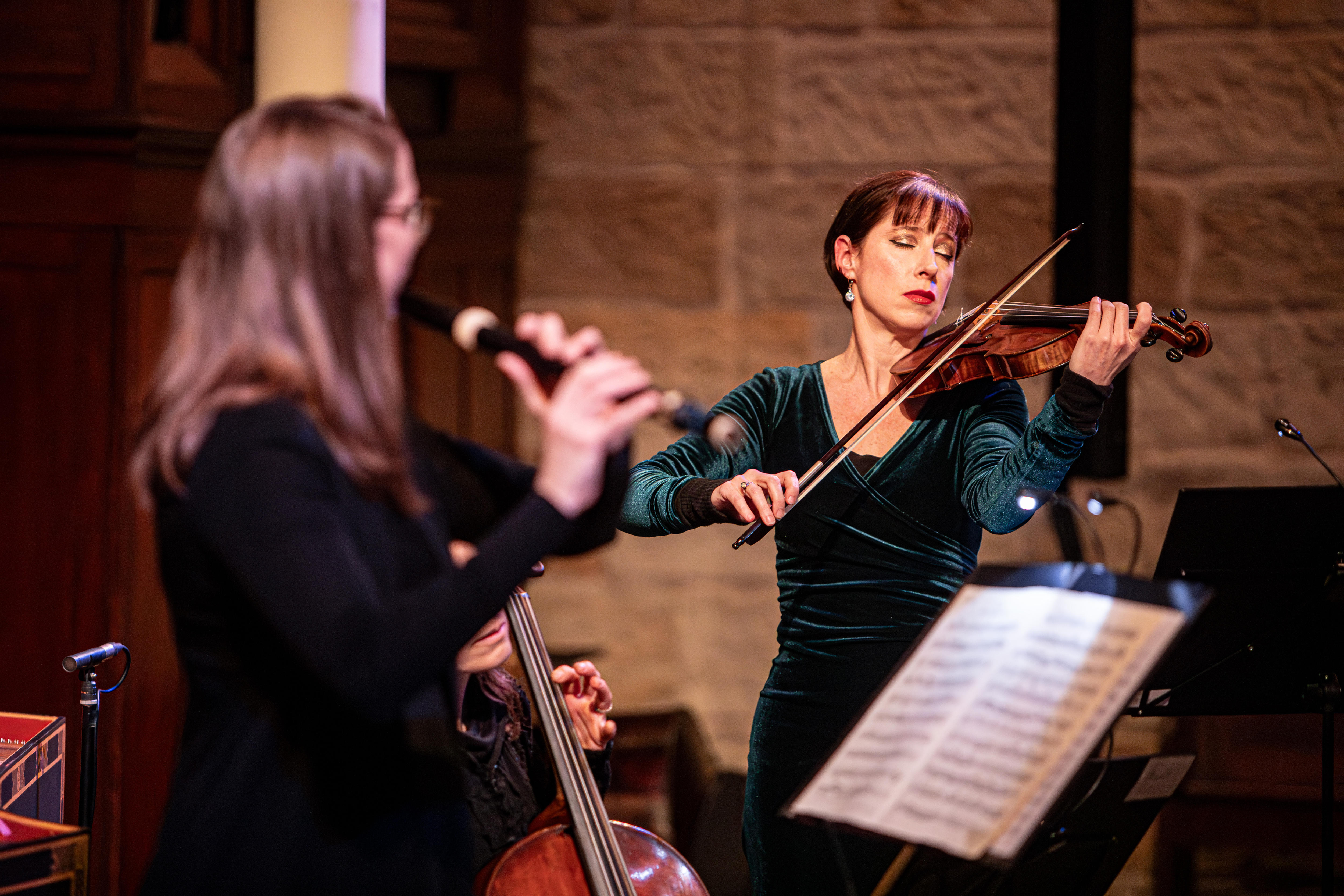 Madeleine Easton performs baroque violin on stage. A baroque flute player is out of focus in the foreground.