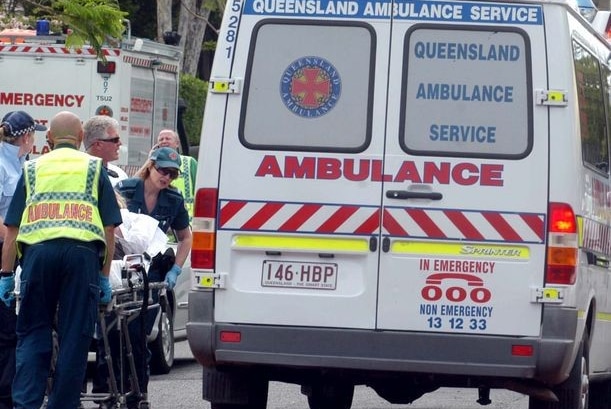 A patient on a stretcher is transferred along a road towards an ambulance by a number of paramedics and a police officer.