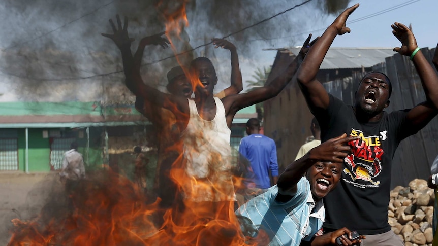 Protesters in Burundi stand behind burning barricade