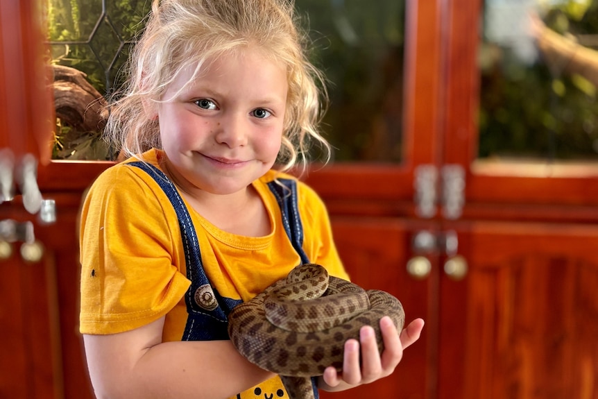 A young girl in a yellow shirt holds a snake. 
