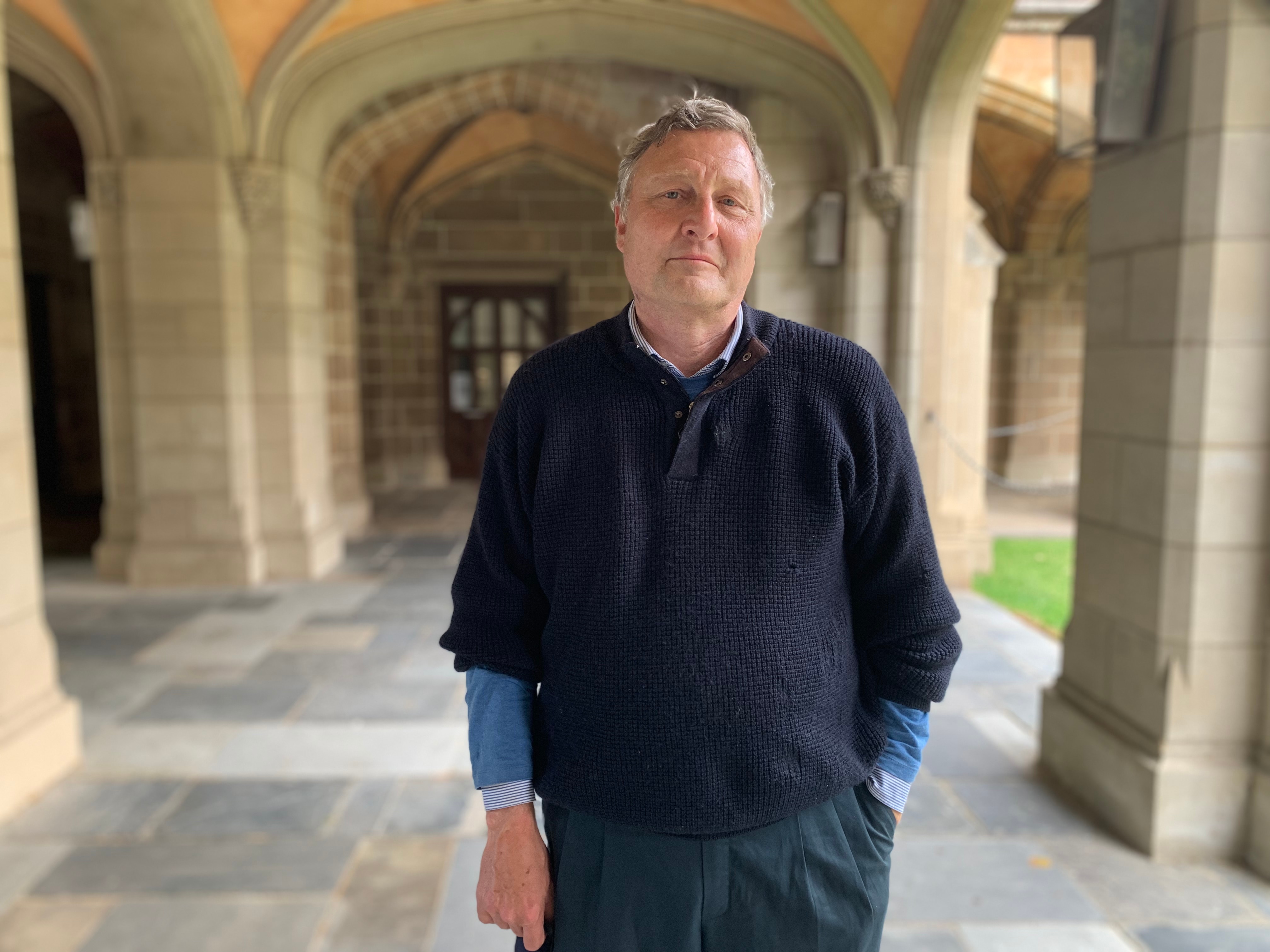 A portrait of Bernd Bartl smiling and standing under a prestigious-looking sandstone archway at the University of Melbourne.