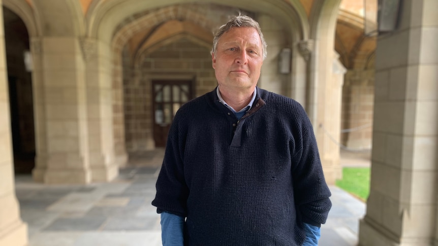 A portrait of Bernd Bartl smiling and standing under a prestigious-looking sandstone archway at the University of Melbourne.