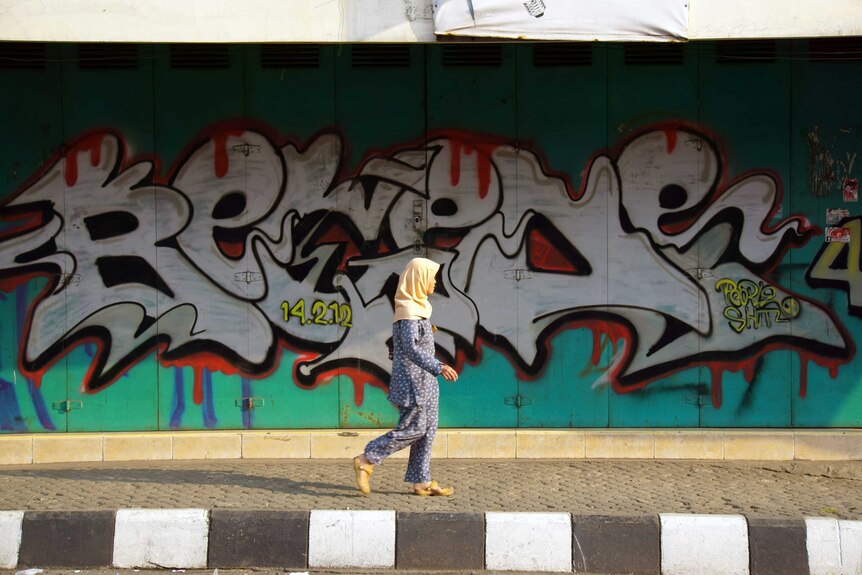 A woman wearing headscarf walking down in frot a graffiti