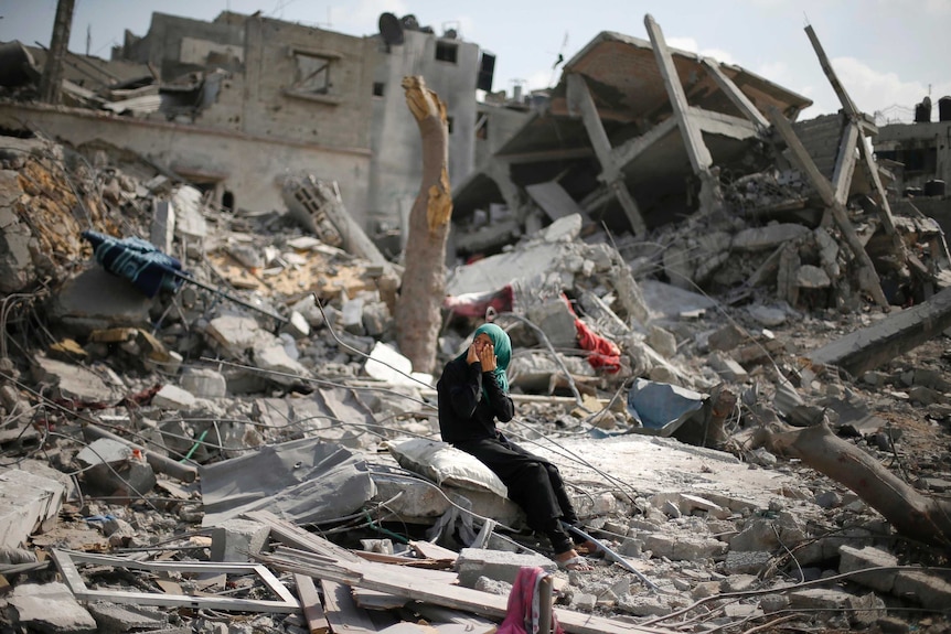 A Palestinian woman holds her face in her hands as she sits on the rubble of her destroyed house after returning to Beit Hanoun town in the northern Gaza Strip.
