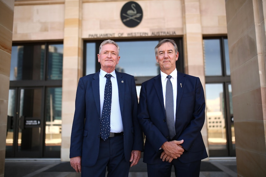 Two men in similar navy blue suits stand outside WA's parliament building