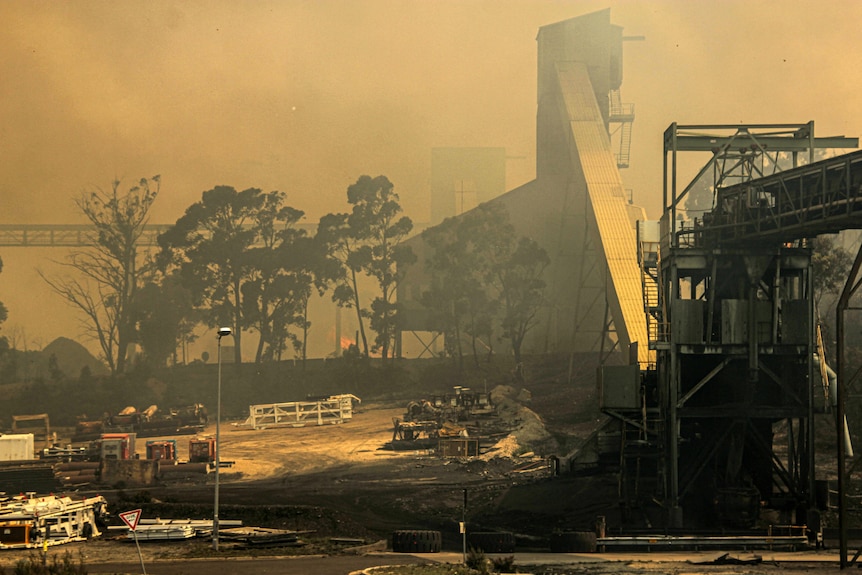 A colliery surrounded by smoke and fire from a bushfire.