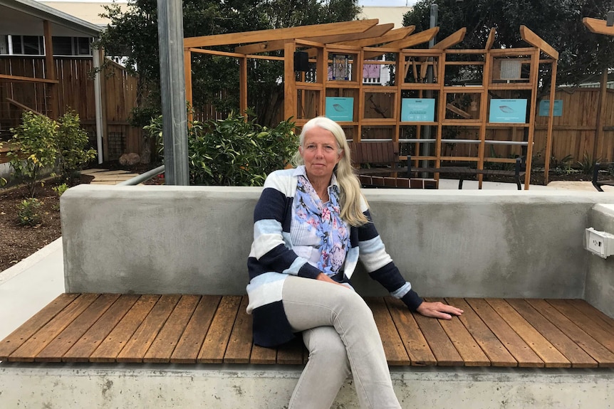 A woman sits on a bench in a garden.