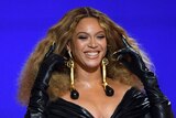 Beyonce smiles on stage in a black dress with large earings