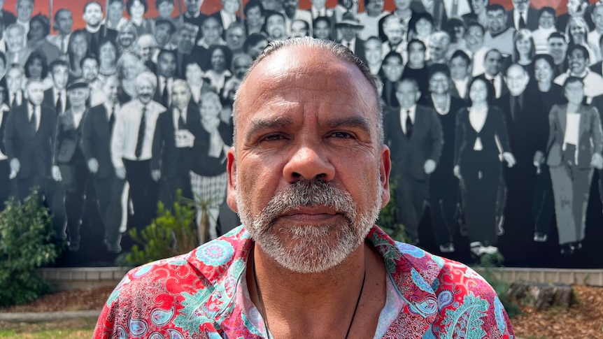 A man stands in front of a wall featuring a mural of protesters. 