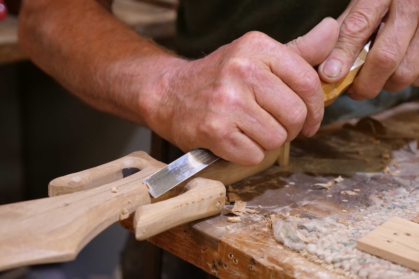 A close up of a mans hands holding a tool, working with timber.