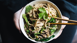 A person holds a bowl of Chinese noodles topped with sesame seeds, mushrooms and Chinese broccoli, for a Lunar New Year meal.