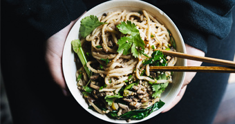 A person holds a bowl of Chinese noodles topped with sesame seeds, mushrooms and Chinese broccoli, for a Lunar New Year meal.