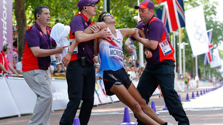 Koichiro Morioka is helped by officials after staggering across the finish line in the 50km walk.