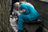 A healthcare worker is hunched over on a park bench