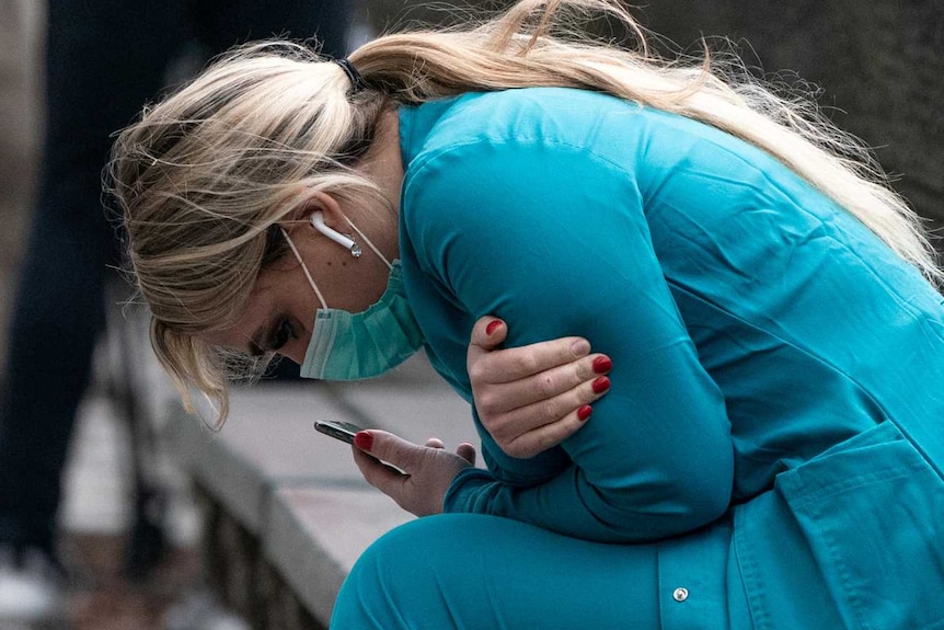 A healthcare worker is hunched over on a park bench