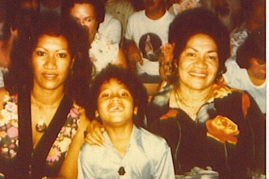 Two Samoan women sit smiling with arm around a young boy. Image looks like its from the 70s.