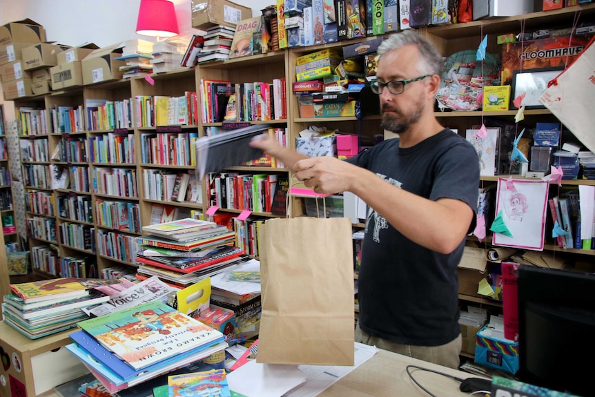 Sam puts a book into a paper bag.