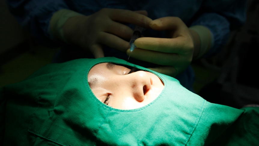 a woman's face can be seen through a surgical gown as hands in gloves are shown behind her