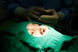 a woman's face can be seen through a surgical gown as hands in gloves are shown behind her