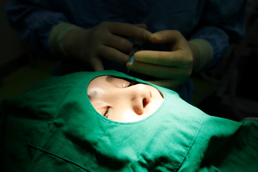 a woman's face can be seen through a surgical gown as hands in gloves are shown behind her