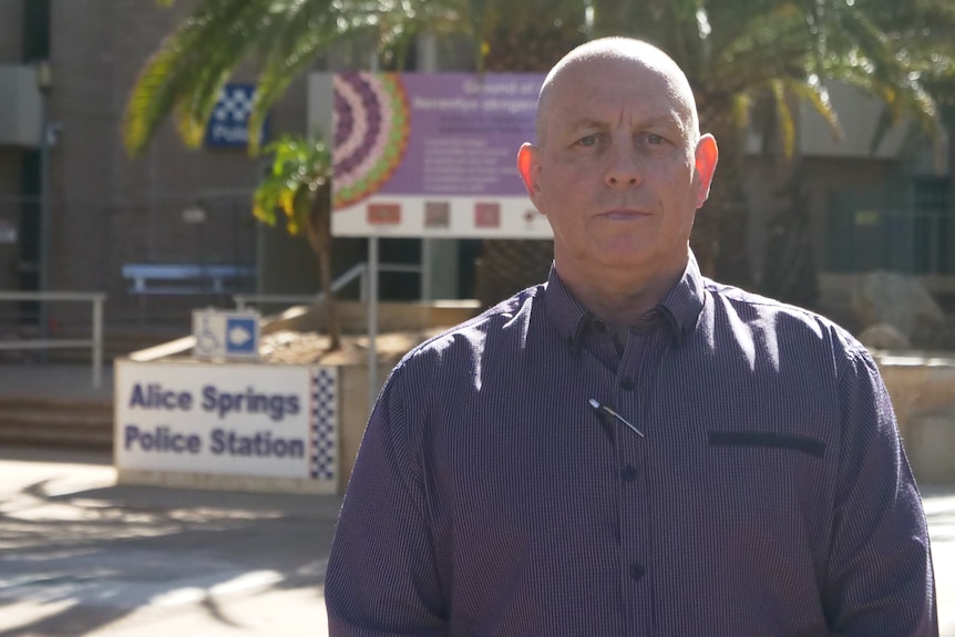 Peter Maley is wearing a long sleeve maroon shirt and looking seriously at the camera. He is at the Alice Springs Police Station