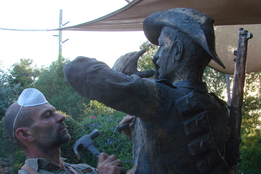 Sculptor Brett Garling using a hammer to shape a bronze statue of a soldier.