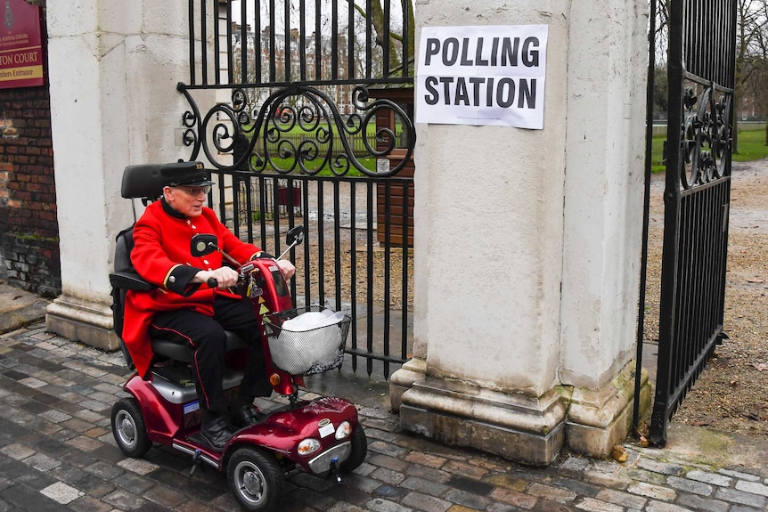 A man on a scooter rides up to a gate to a polling station in the UK.
