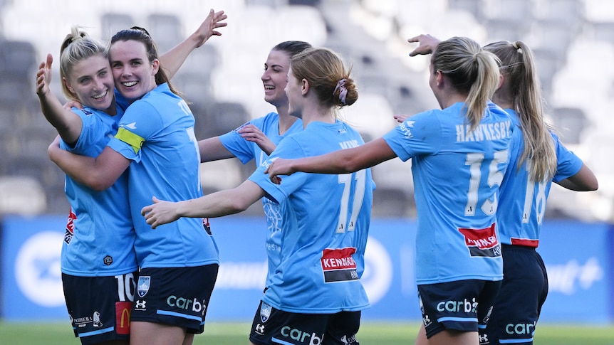 Six Sydney FC A-League Women players embrace as they celebrate a goal.