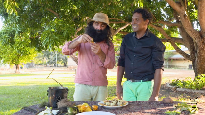 Two men standing outdoors at table cooking